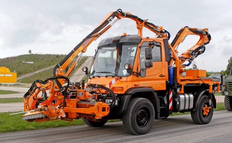 Road maintenance vehicle with mowing arms
